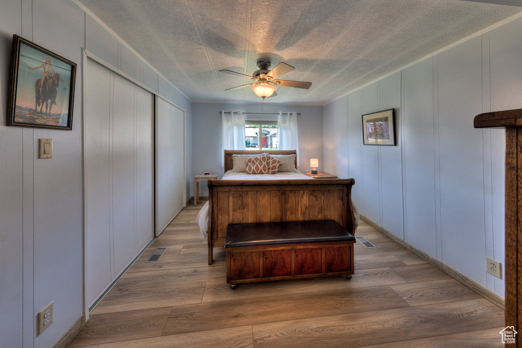 Bedroom with a decorative wall, light wood-style flooring, a closet, ceiling fan, and a textured ceiling