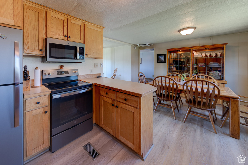 Kitchen featuring stainless steel appliances, a peninsula, light wood-style floors, and light countertops
