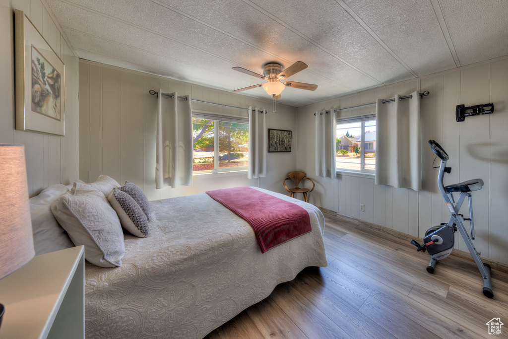 Bedroom featuring light wood-type flooring, multiple windows, a textured ceiling, a decorative wall, and a ceiling fan