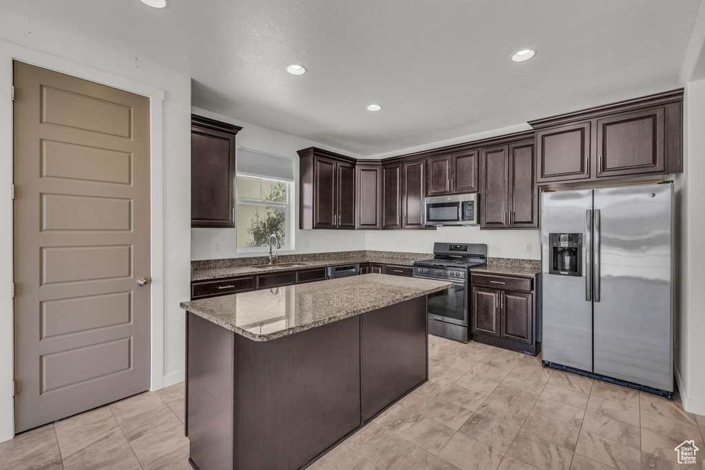 Kitchen with appliances with stainless steel finishes, dark brown cabinetry, light stone countertops, recessed lighting, and a center island