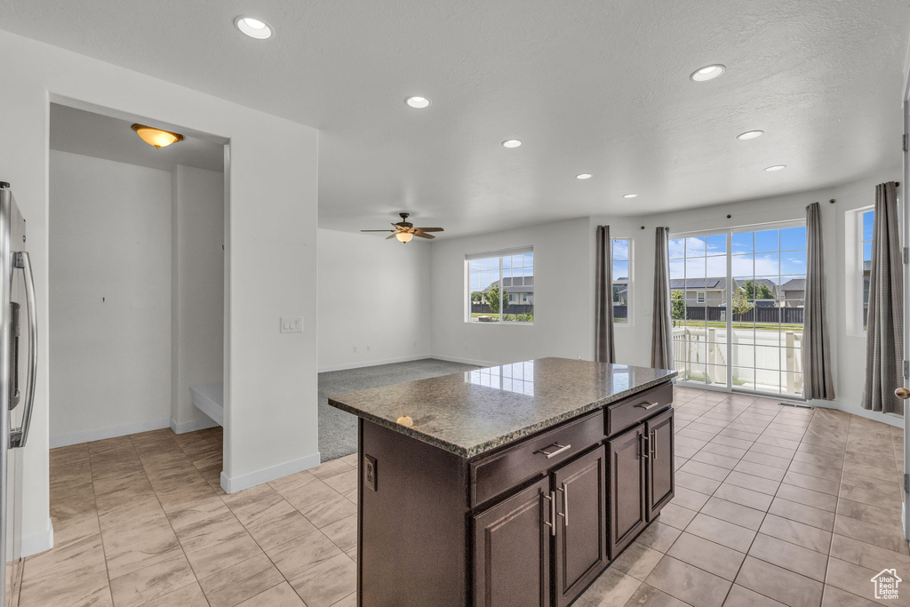 Kitchen with recessed lighting, a ceiling fan, dark brown cabinets, light stone counters, and a center island