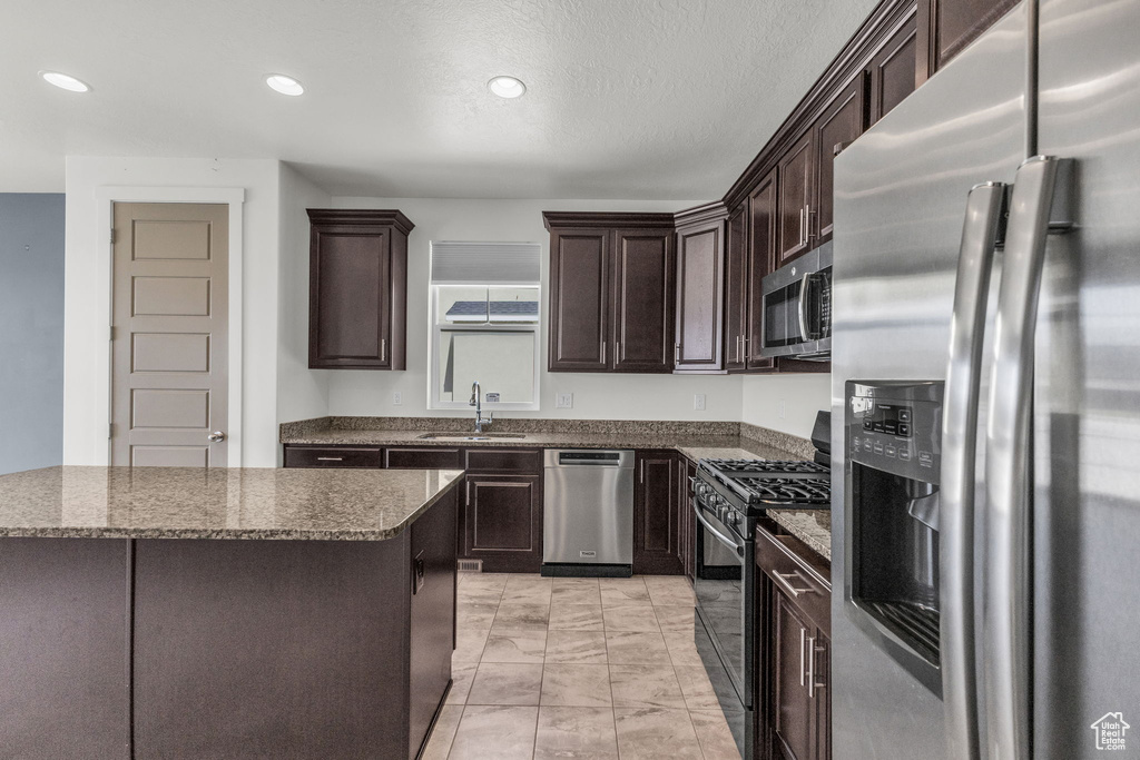 Kitchen with appliances with stainless steel finishes, dark brown cabinetry, dark stone countertops, recessed lighting, and light marble finish flooring