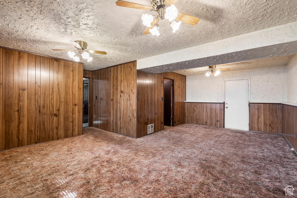 Spare room with ceiling fan, wooden walls, carpet flooring, wainscoting, and a textured ceiling