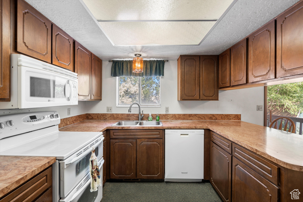 Kitchen with white appliances, a sink, a textured ceiling, a peninsula, and light countertops