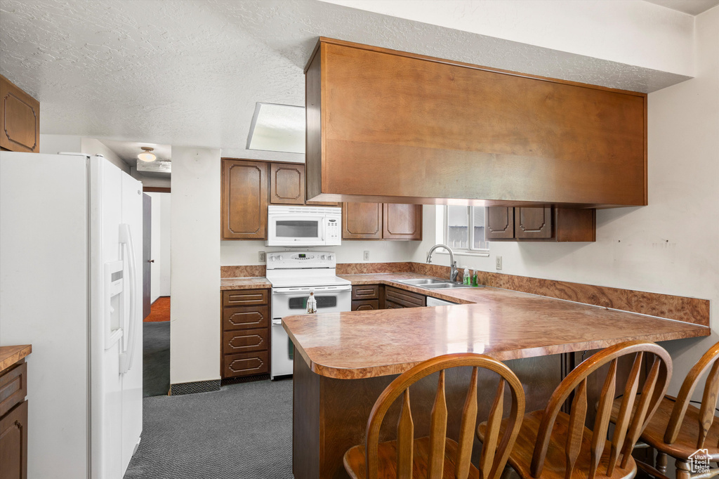 Kitchen featuring white appliances, a sink, a peninsula, dark colored carpet, and a breakfast bar area