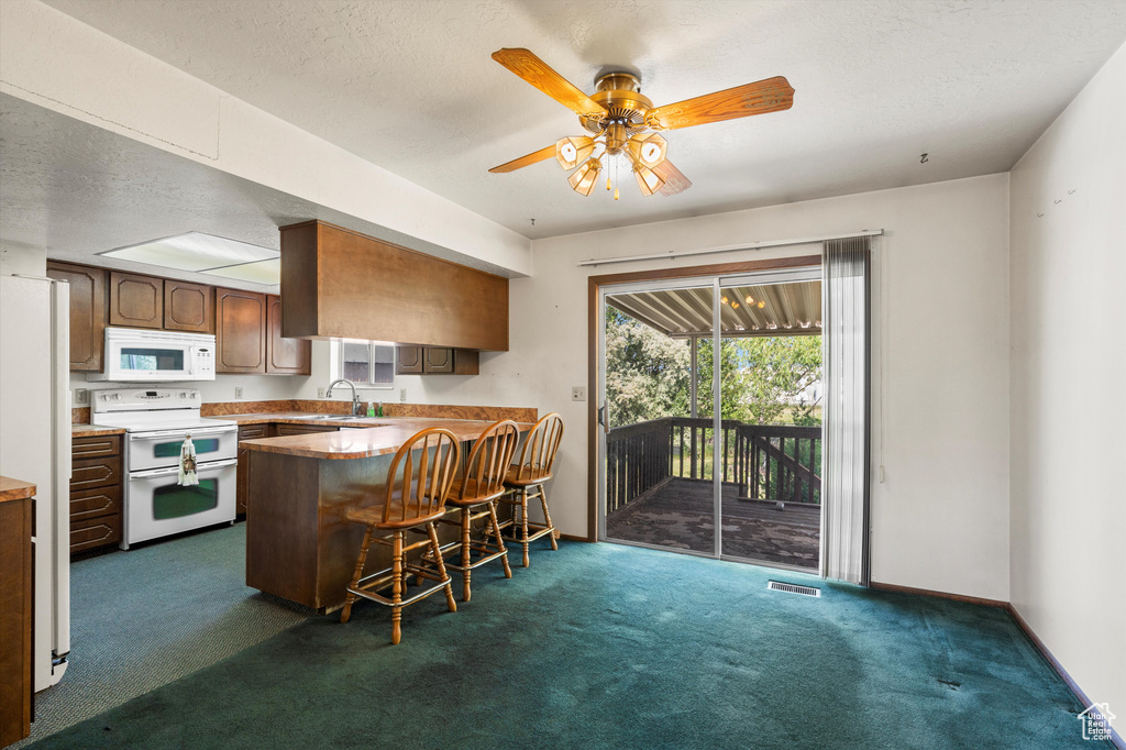 Kitchen featuring white appliances, a sink, a peninsula, dark colored carpet, and a kitchen breakfast bar
