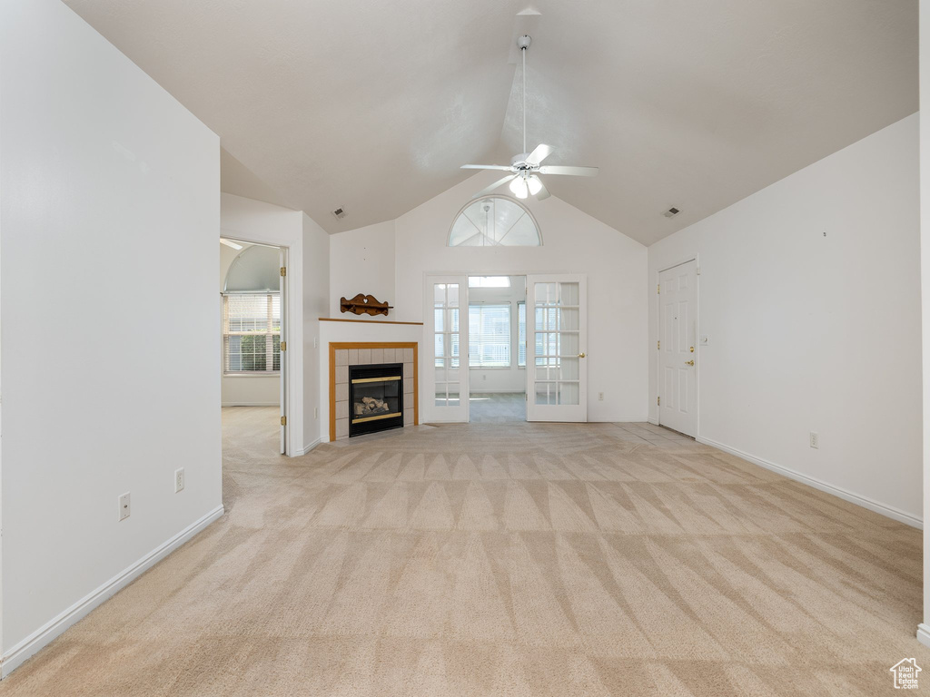 Unfurnished living room featuring plenty of natural light, light colored carpet, ceiling fan, and high vaulted ceiling