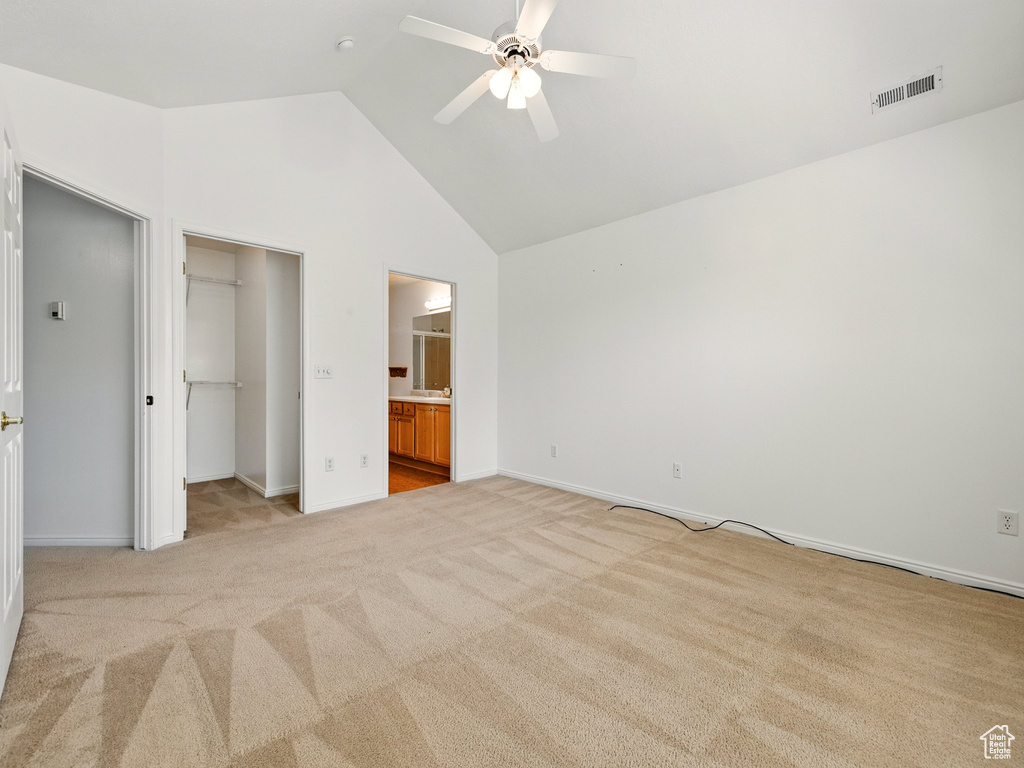 Unfurnished bedroom featuring high vaulted ceiling, a walk in closet, light colored carpet, ensuite bathroom, and a ceiling fan