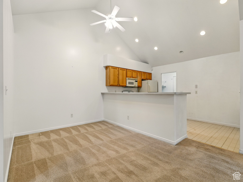 Kitchen with white appliances, light colored carpet, high vaulted ceiling, brown cabinetry, and recessed lighting