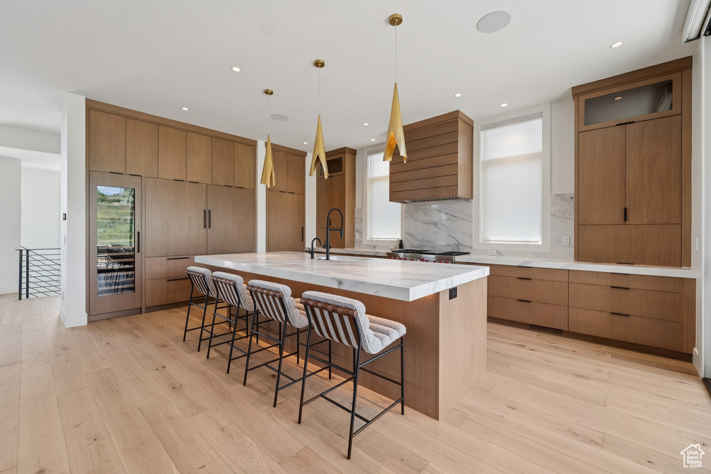 Kitchen featuring wall chimney exhaust hood, light wood finished floors, a spacious island, a breakfast bar area, and recessed lighting