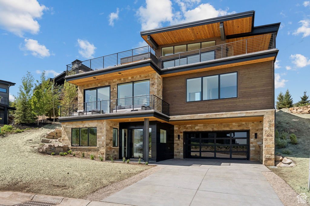 Contemporary home featuring a balcony, driveway, a garage, and stone siding