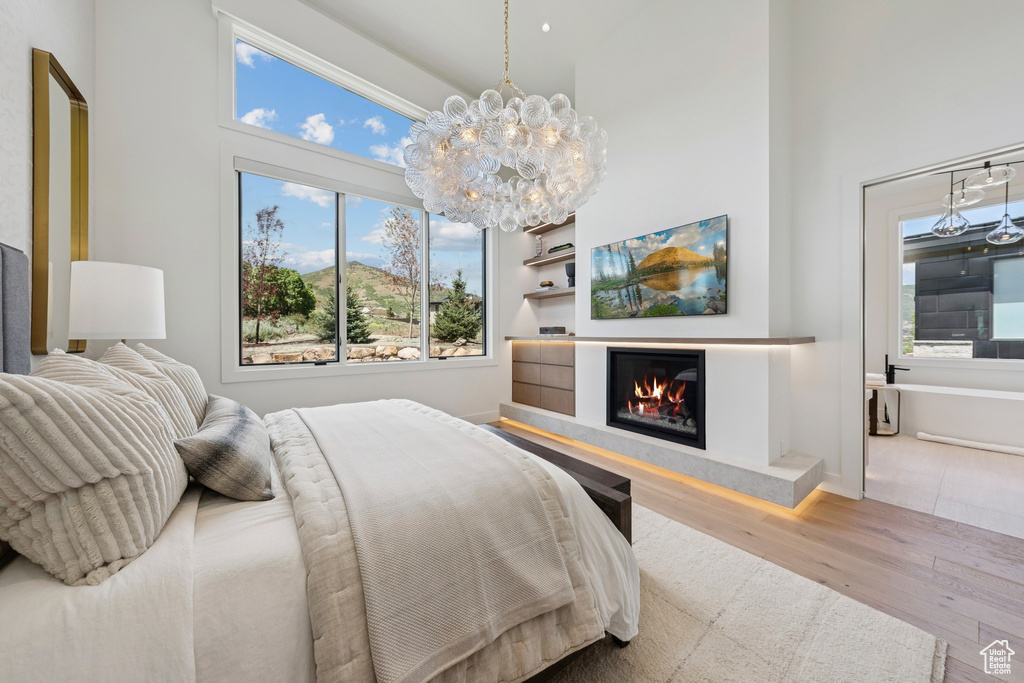 Bedroom with wood finished floors, a high ceiling, a glass covered fireplace, and a chandelier