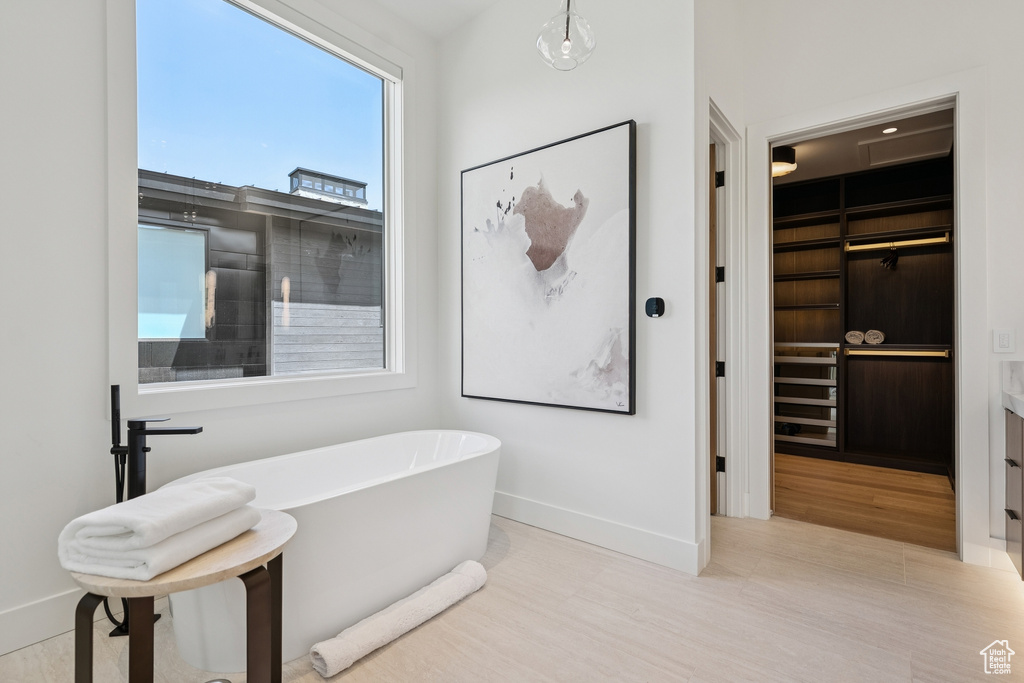 Full bathroom featuring a soaking tub, a walk in closet, and wood finished floors