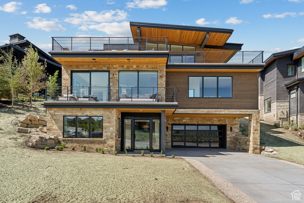 Modern home with a balcony, concrete driveway, and stone siding