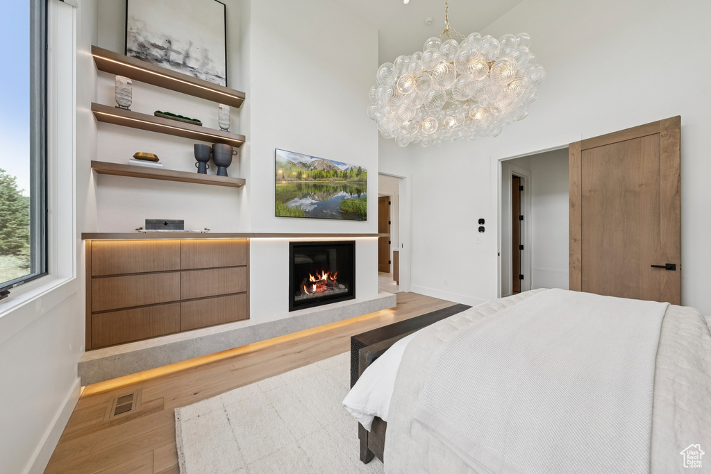 Bedroom featuring wood finished floors, a high ceiling, a glass covered fireplace, and a chandelier