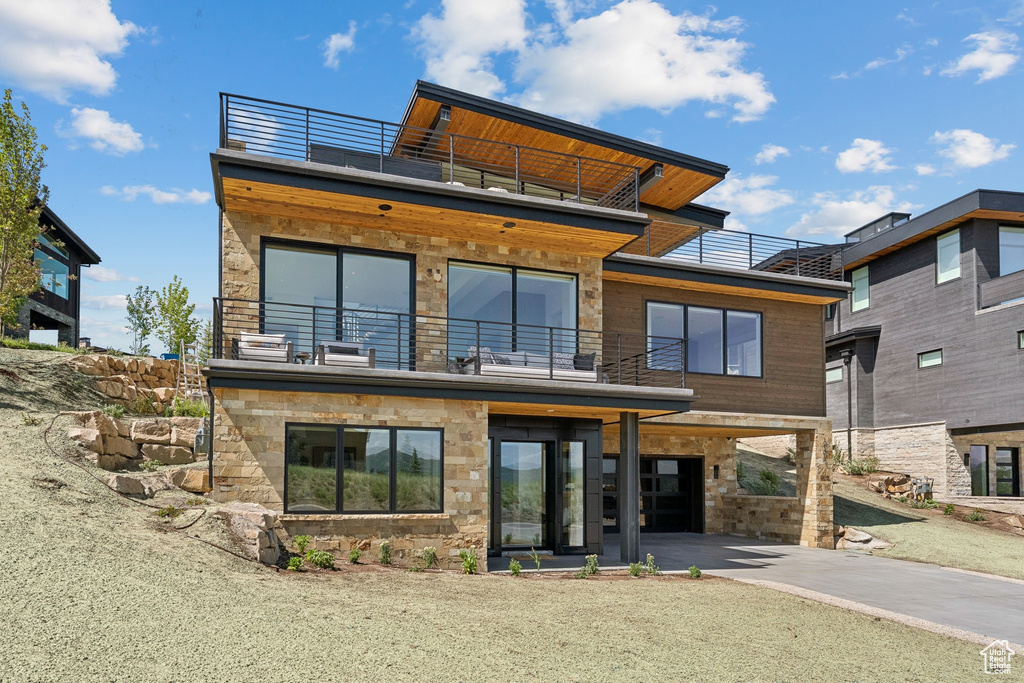 Back of property featuring a balcony, concrete driveway, and stone siding