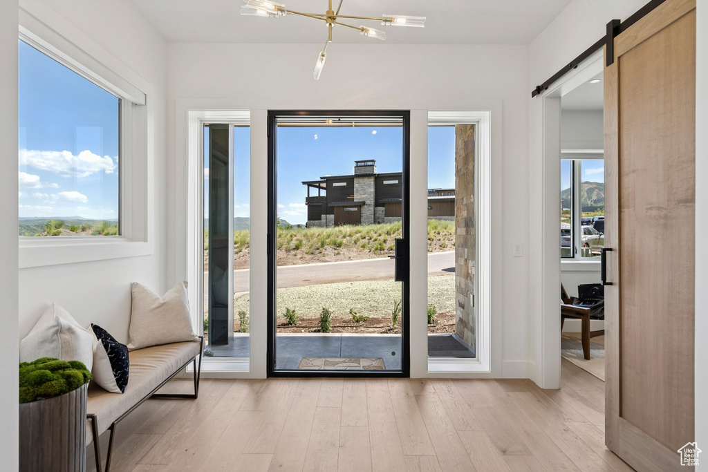 Doorway to outside featuring light wood-type flooring, a barn door, and a chandelier