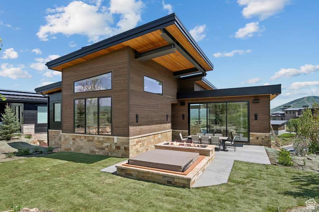 Rear view of house featuring stone siding, a patio, and a yard