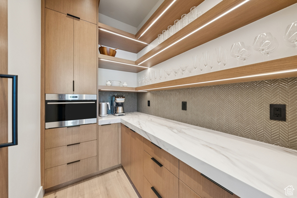 Kitchen with stainless steel oven, open shelves, light stone counters, light wood-style floors, and light brown cabinetry