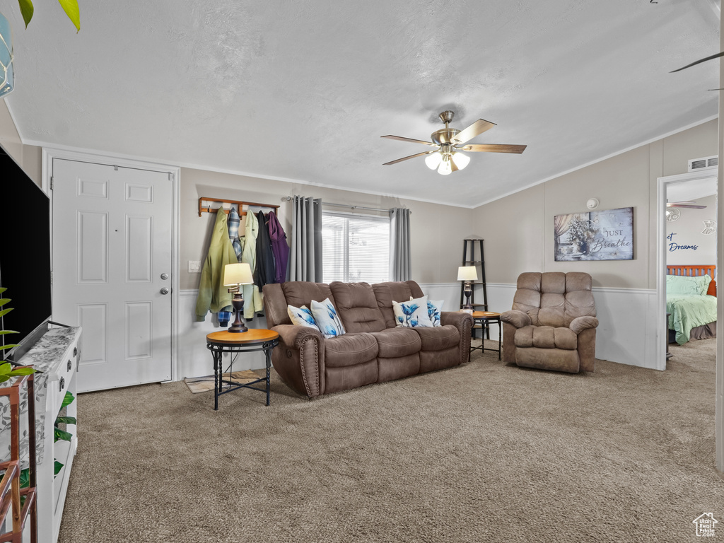 Living room with a ceiling fan, carpet floors, lofted ceiling, crown molding, and wainscoting