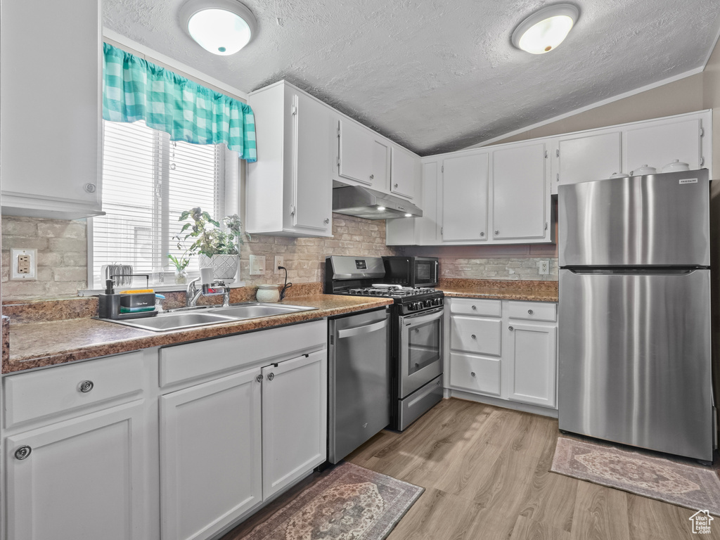 Kitchen with appliances with stainless steel finishes, a sink, lofted ceiling, a textured ceiling, and under cabinet range hood