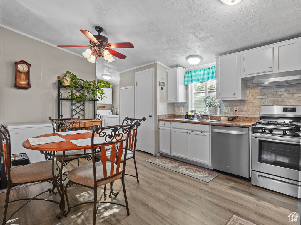 Kitchen with appliances with stainless steel finishes, under cabinet range hood, decorative backsplash, a ceiling fan, and light wood-style floors