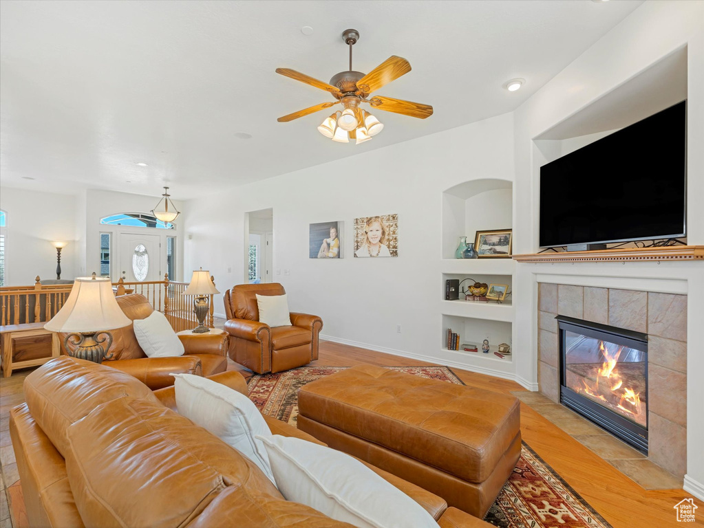 Living area with built in features, light wood-type flooring, a ceiling fan, and a tiled fireplace