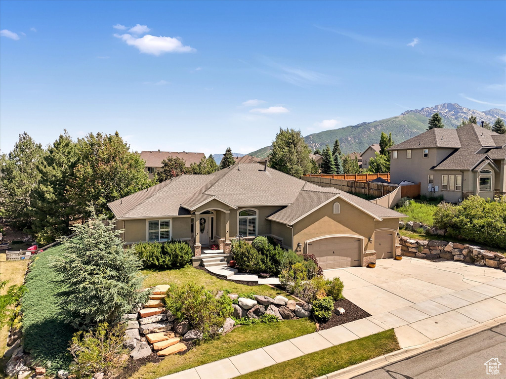 View of front of property with an attached garage, stucco siding, a mountain view, driveway, and roof with shingles