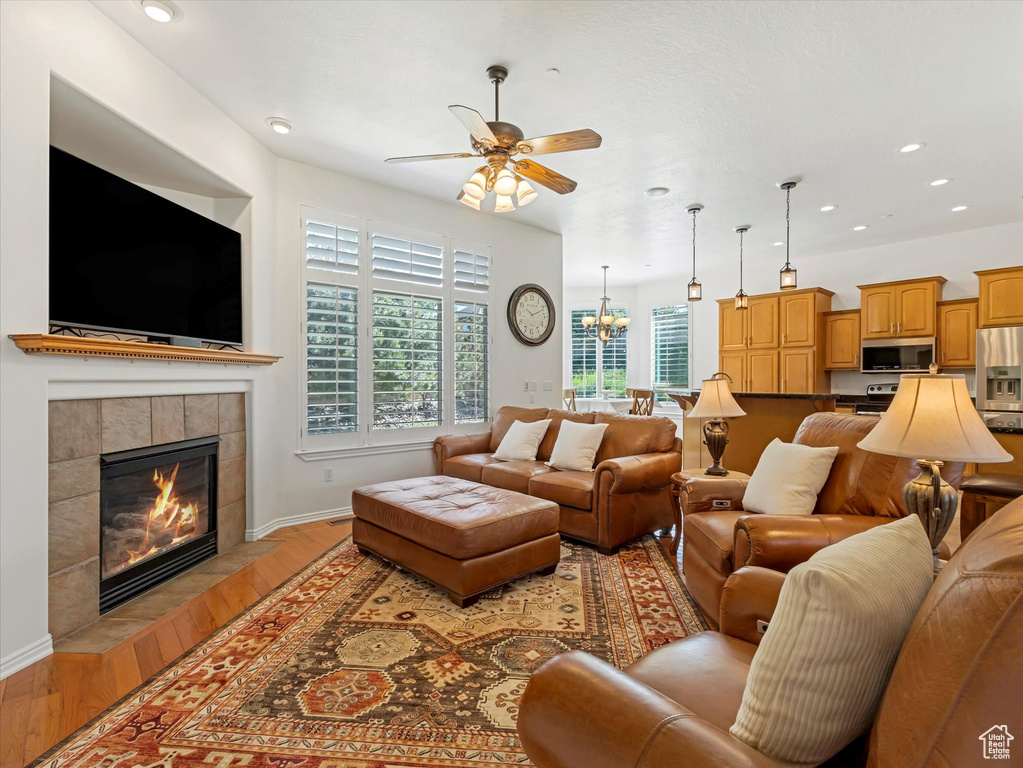 Living area featuring a ceiling fan, a tile fireplace, light wood-type flooring, recessed lighting, and a chandelier