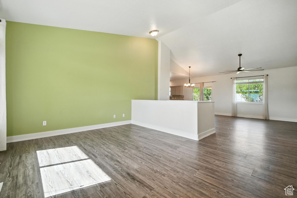 Unfurnished living room with a chandelier, vaulted ceiling, a ceiling fan, and dark wood finished floors