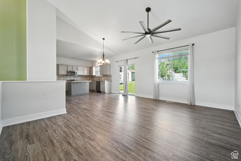 Unfurnished living room featuring a ceiling fan, a chandelier, dark wood-style floors, and high vaulted ceiling