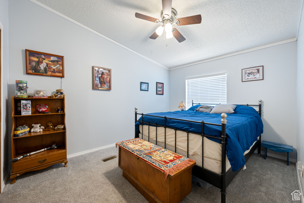 Carpeted bedroom featuring lofted ceiling, a textured ceiling, ornamental molding, and a ceiling fan