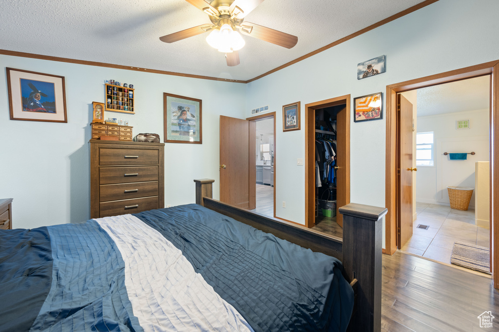 Bedroom with wood finished floors, a spacious closet, crown molding, a closet, and connected bathroom