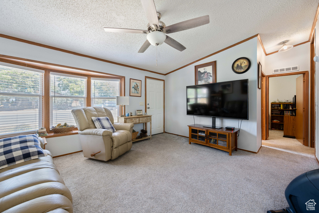 Carpeted living area featuring ornamental molding, ceiling fan, a textured ceiling, and vaulted ceiling