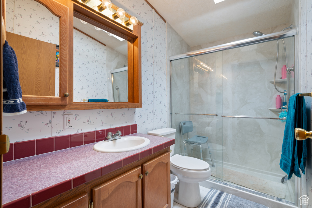 Full bath featuring wallpapered walls, vanity, and a stall shower
