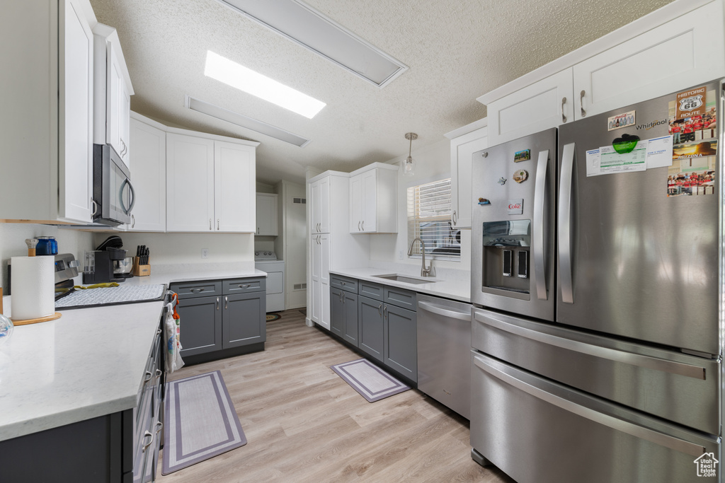 Kitchen featuring appliances with stainless steel finishes, light wood-type flooring, a textured ceiling, and white cabinets