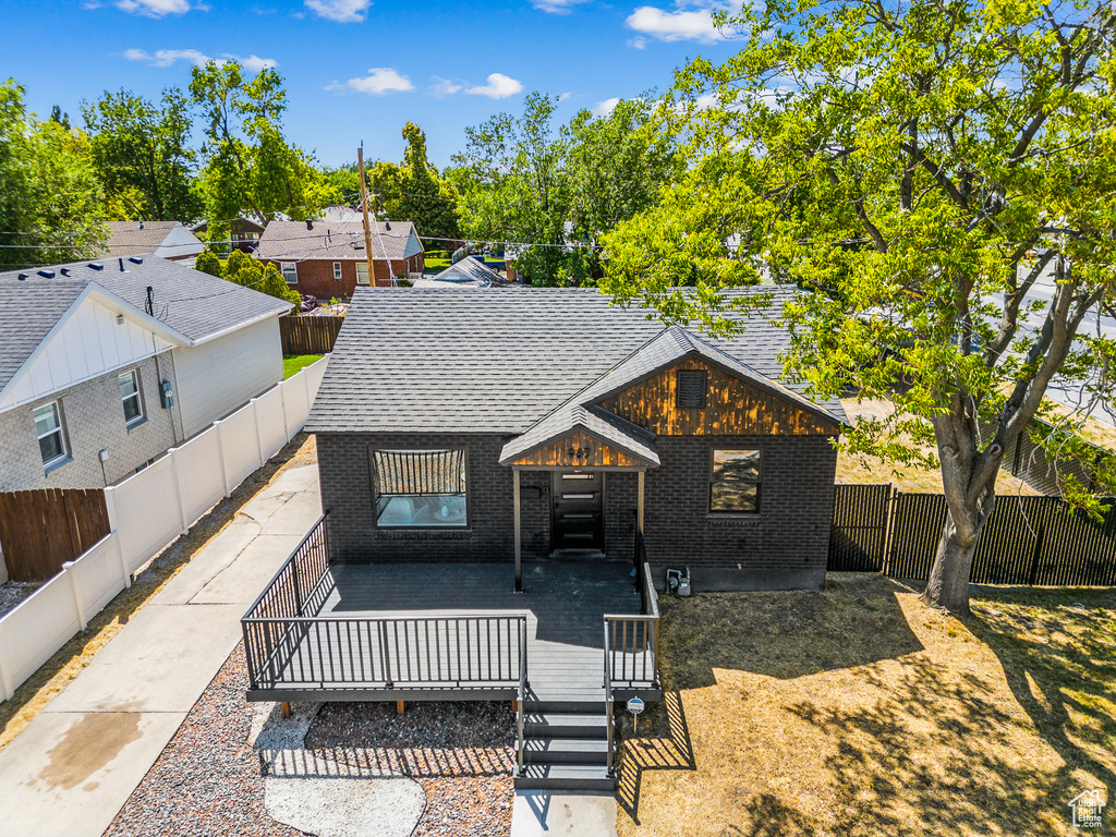View of front of property featuring brick siding, a deck, roof with shingles, and a fenced backyard