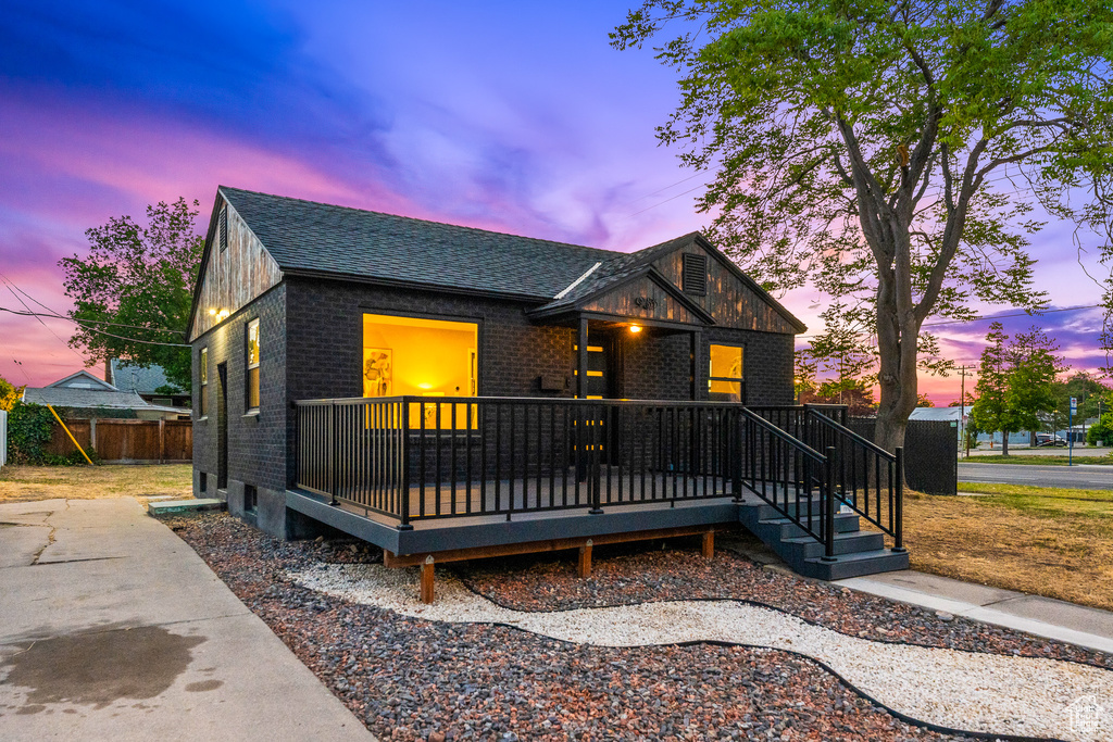 View of front of house with brick siding, a shingled roof, and a deck