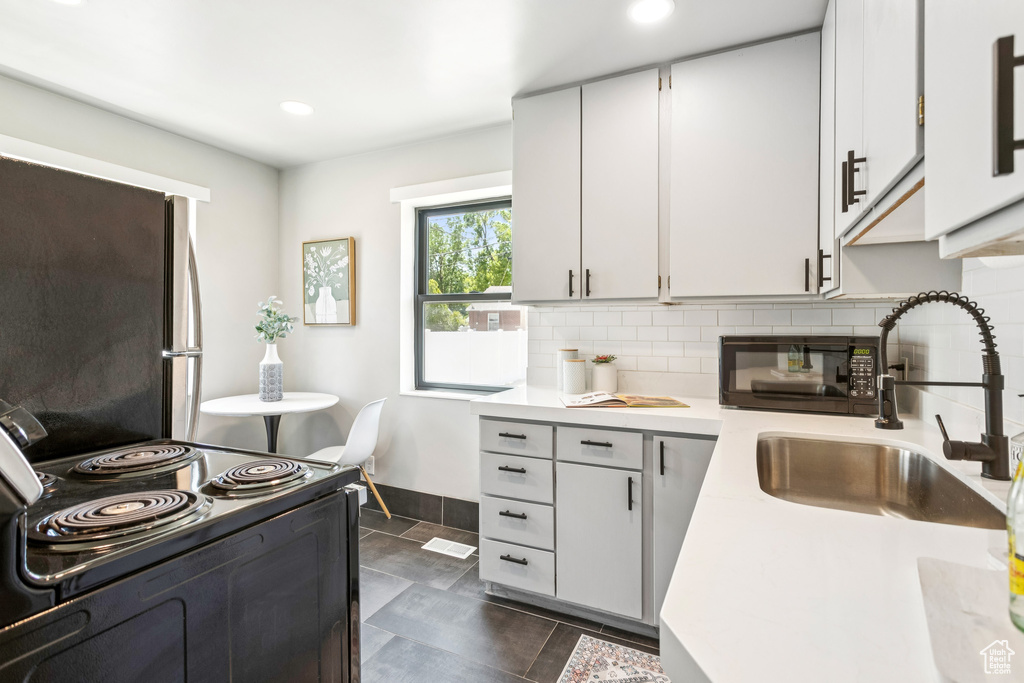 Kitchen with black electric range, light countertops, backsplash, freestanding refrigerator, and recessed lighting