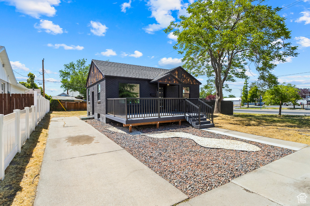 View of front of home featuring a deck, brick siding, and roof with shingles