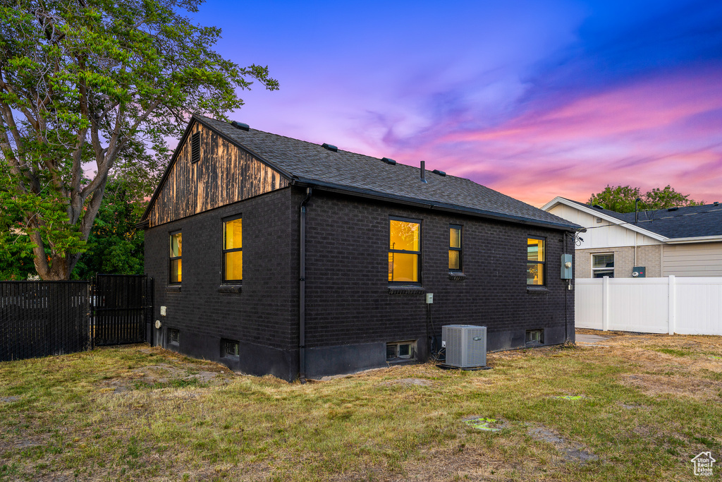 Back of house at dusk with a fenced backyard, brick siding, and a shingled roof