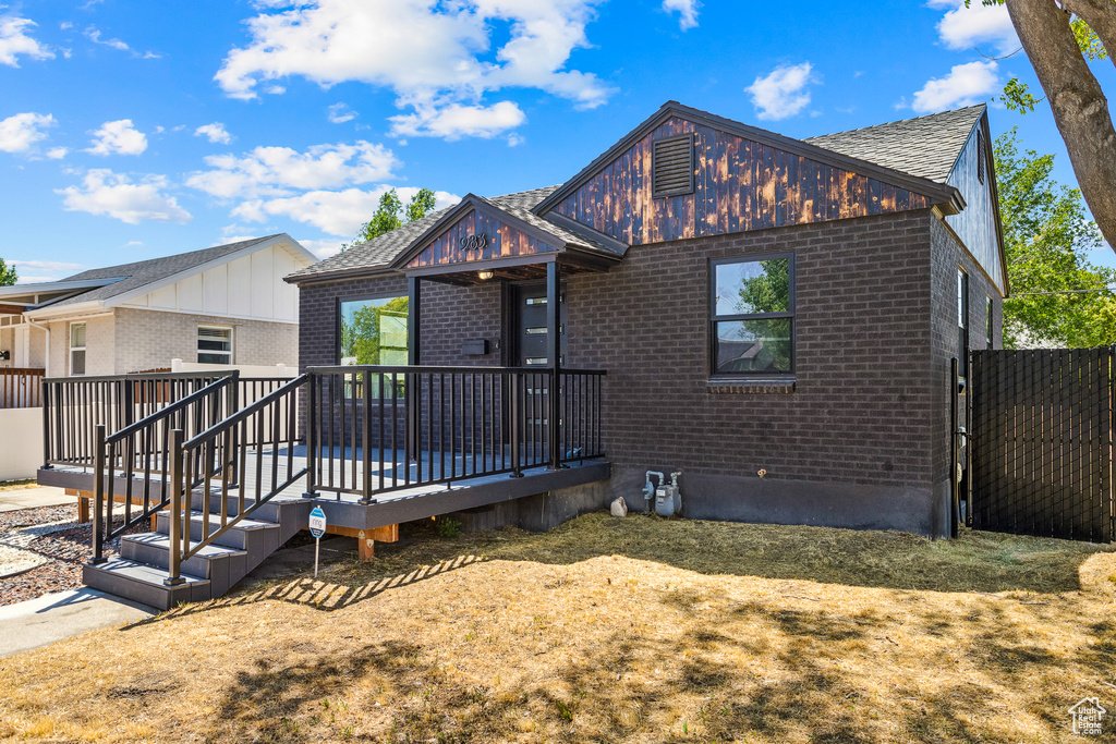 View of front of house featuring brick siding, roof with shingles, and a wooden deck