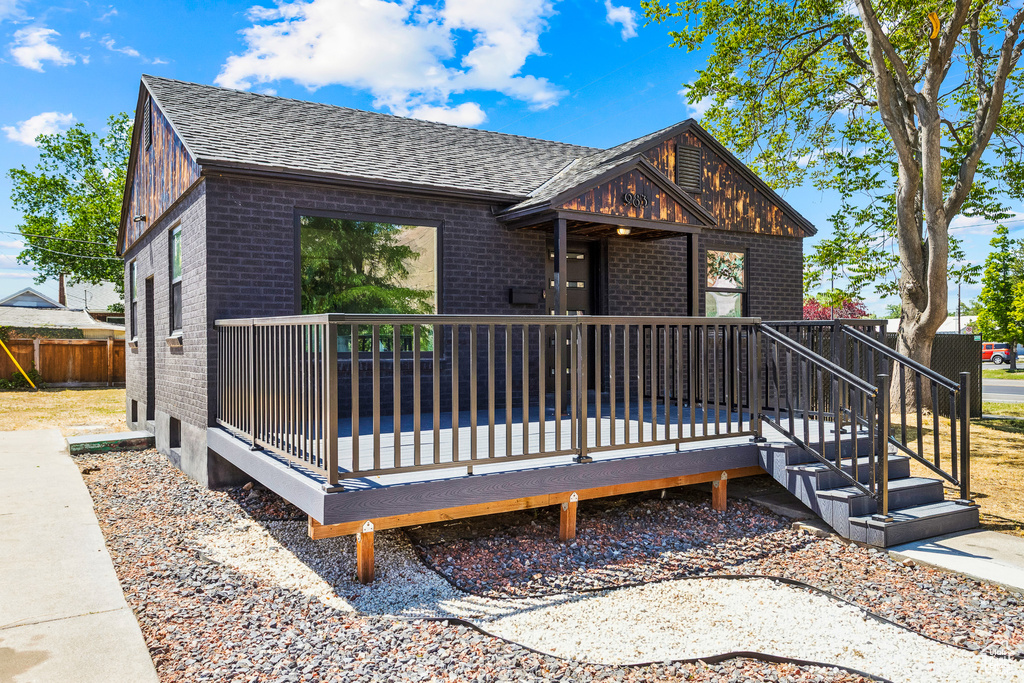 View of front of home featuring brick siding, a shingled roof, and a deck