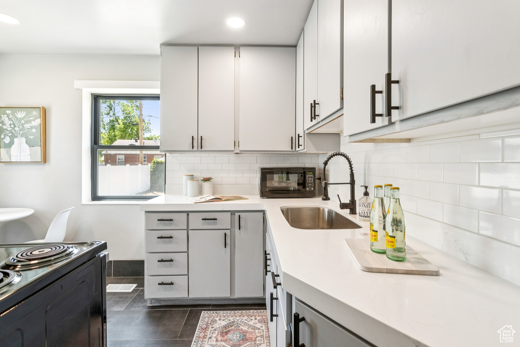 Kitchen featuring light countertops, black appliances, tasteful backsplash, dark tile patterned flooring, and recessed lighting