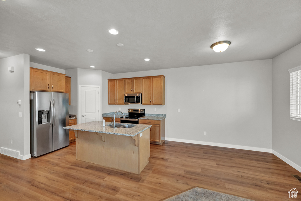 Kitchen featuring stainless steel appliances, light stone counters, recessed lighting, light wood-type flooring, and a kitchen bar