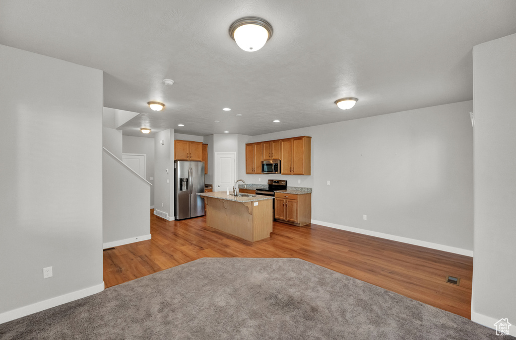 Kitchen with appliances with stainless steel finishes, a breakfast bar, open floor plan, an island with sink, and wood finished floors