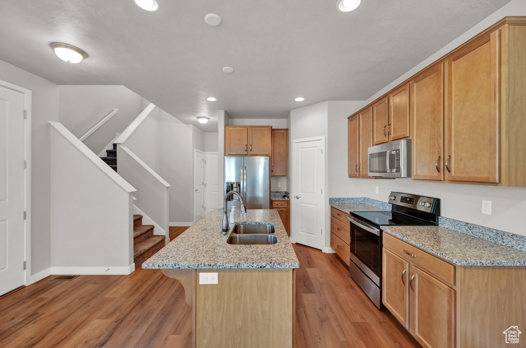 Kitchen with appliances with stainless steel finishes, light wood-style flooring, recessed lighting, and light stone counters