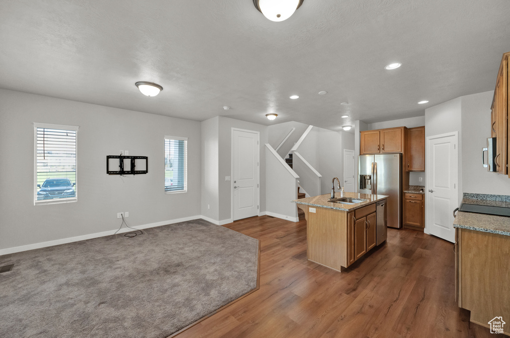 Kitchen featuring appliances with stainless steel finishes, a kitchen island with sink, recessed lighting, dark wood-style flooring, and light stone countertops
