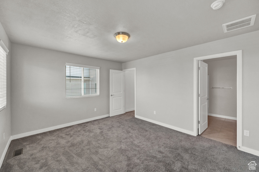 Unfurnished bedroom with carpet floors, multiple windows, and a walk in closet