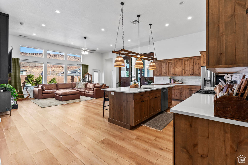 Kitchen with stainless steel appliances, light countertops, open floor plan, a ceiling fan, and a kitchen island with sink